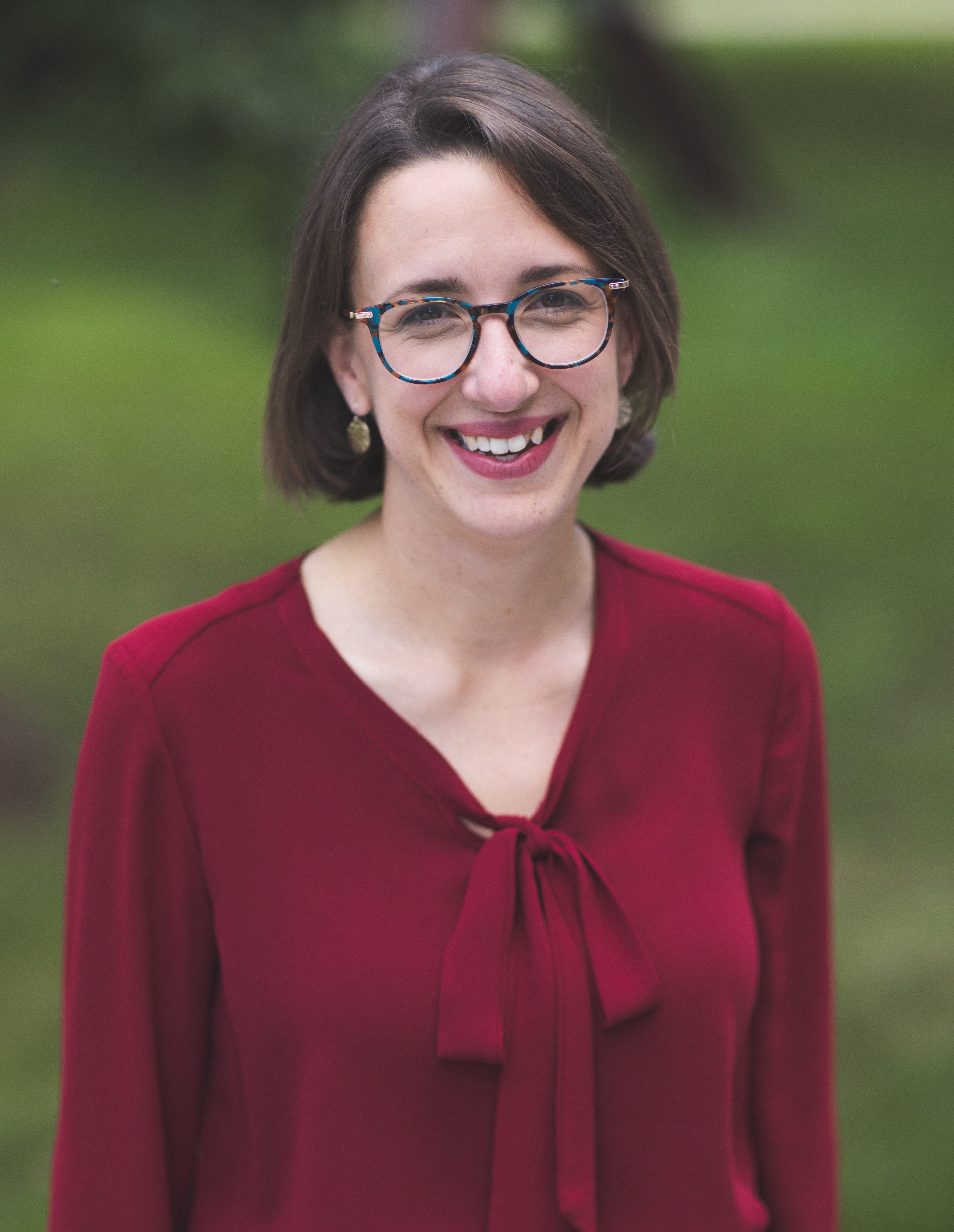 A picture of a woman smiling, wearing a red shirt and glasses. 